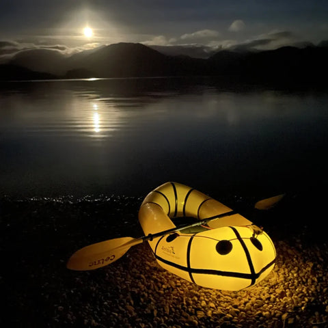 Opplyst Anfibio Alpha XC på stranden under fullmåne. Viser packraftens lave vekt og portabilitet for nattlige ekspedisjoner og villmarksliv. Foto: Nicholas Brooks.
