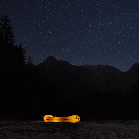 Opplyst gul Anfibio Omega C2 packraft på elvebredd under en klar stjernehimmel i fjellet. Perfekt for ekspedisjoner og camping. Foto: Lisa Kristin Schröter.