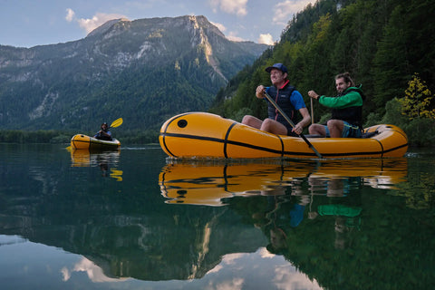 To menn som padler en gul Anfibio Omega C2 packraft som kano på et krystallklart fjellvann. Stabil og romslig tomanns packraft. Foto: Lisa Kristin Schröter.