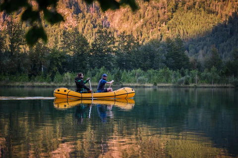 Sidevisning av Anfibio Omega C2 packraft i bevegelse på vannet med to padlere. Viser den strømlinjeformede formen og sorte detaljer. Foto: Lisa Kristin Schröter.