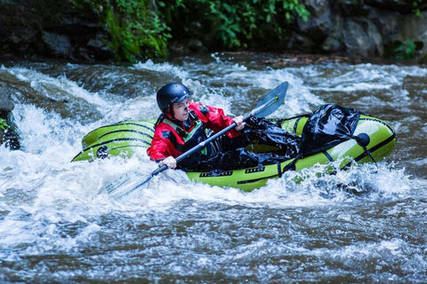 Padler i en grønn Anfibio Revo CL+ packraft som manøvrerer gjennom hvitt vann. Viser det integrerte spruttrekket og den stive TwinTube-konstruksjonen. Foto: Anfibio Packrafting.