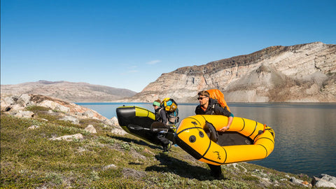To padlere bærer sine oppblåste Anfibio Sigma TX packrafts langs kanten av et fjellvann. Viser båtens lave vekt for transport mellom vannveier. Foto: Anfibio