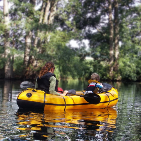 En mor og et barn padler sammen i en gul Anfibio Sigma TX på en rolig elv. En trygg og stabil packraft perfekt for familieopplevelser. Foto: Sven Schellin.