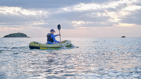En person padler en Anfibio Sigma TXL på åpent vann mot en liten øy i solnedgang. En lett og bærbar packraft for tur. Foto: Anfibio Packrafting.