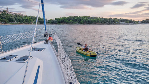 En person padler en grønn Anfibio Sigma TXL packraft ved siden av en seilbåt. Ideell som lettbåt og tender for båtfolk. Foto: Anfibio Packrafting.