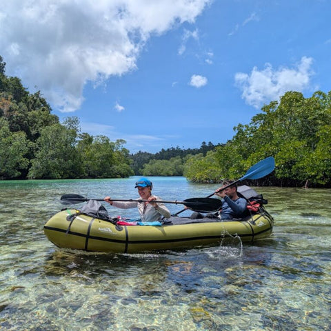 To personer i en grønn Anfibio Rebel Duo packraft med Tube Bags i krystallklart vann. Viser packraftens kapasitet for ekspedisjoner og bagasjeoppbevaring. Foto: Anfibio Packrafting.